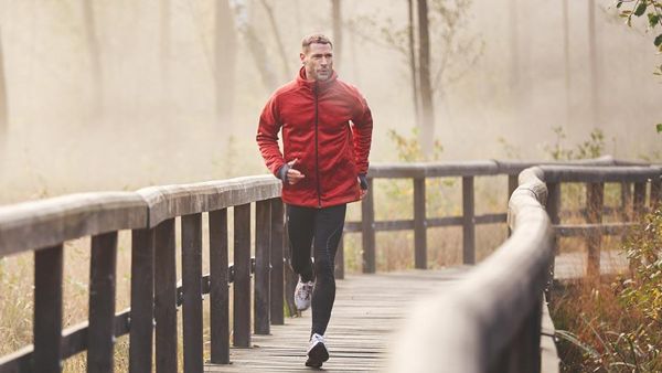 Man jogt over een voetgangersbrug in de ochtendmist in een rood jack.