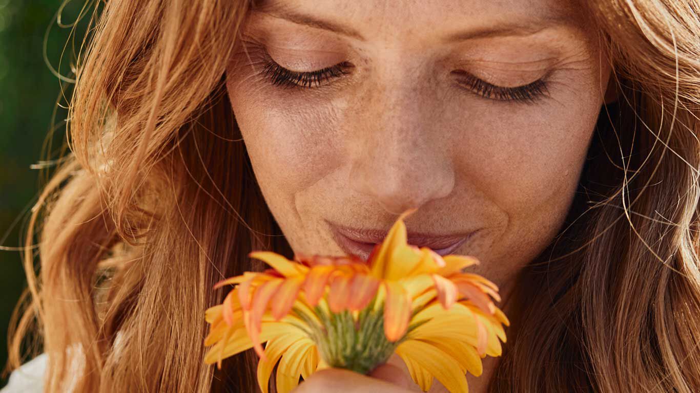 Een jonge vrouw ruikt aan een calendula bloem.
