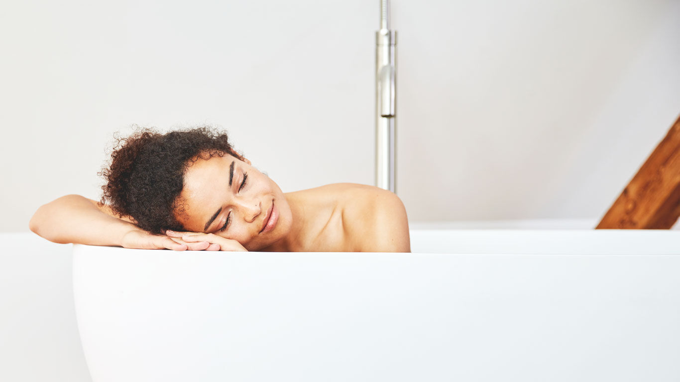 Une femme dans la baignoire pose sa tête sur le rebord de la baignoire.