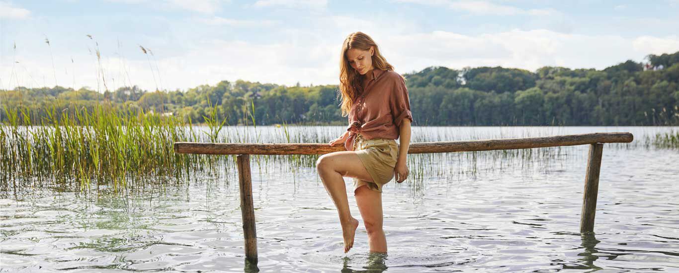 Een vrouw staat bijna tot haar knie in een meer en symboliseert het watertrappelen.