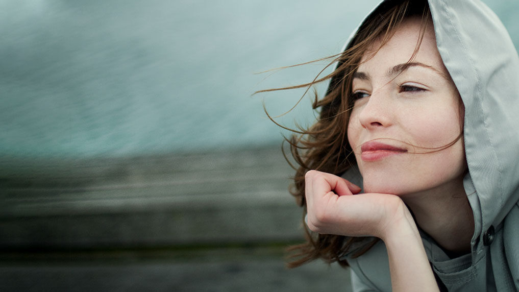 Vrouw laat haar kin op haar hand rusten en geniet van de vrijheid in de wind. Haar haren wapperen in de wind.