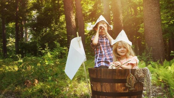 Meisje en jongen in een houten vat in het bos spelen piraten.