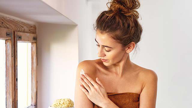 Femme avec un chignon en train d'appliquer de la crème. 