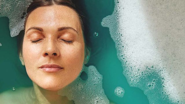 Une femme est allongée jusqu'à la racine des cheveux dans une baignoire d'eau bleue.