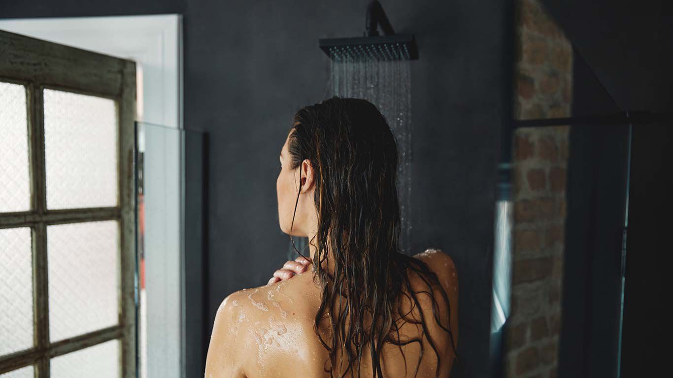 Donkerharige vrouw met nat haar onder de douche. Van achteren gezien.