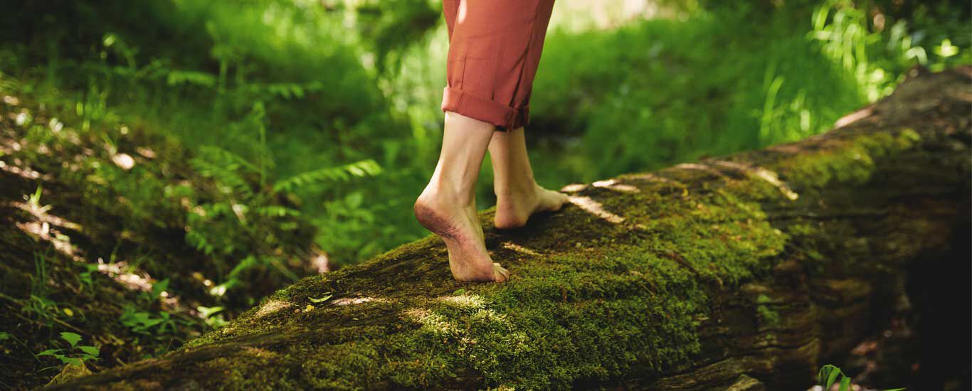 Femme marchant sur un tronc d'arbre dans la forêt, l'image étant composée d'un gros plan sur ses pieds.
