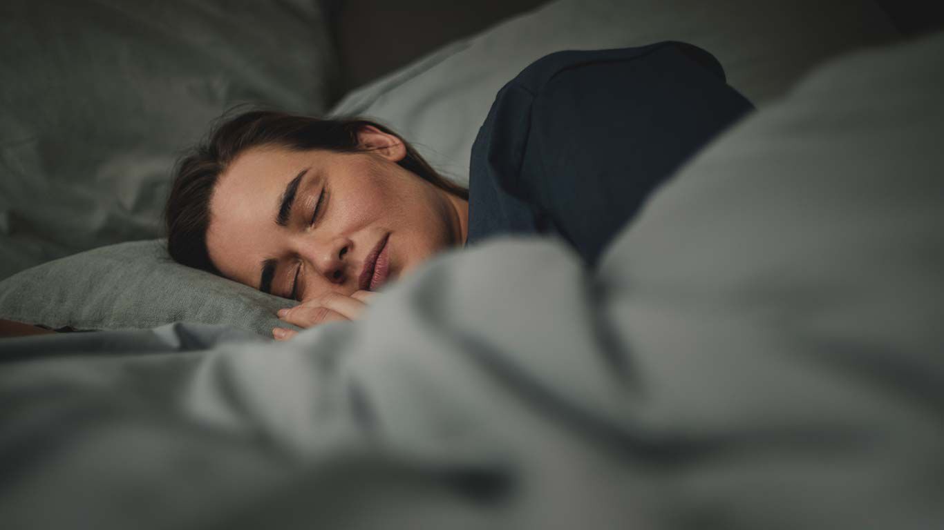 Als we slapen, is ons lichaam, in zekere zin, zijn systemen aan het herijken. Vrouw ligt in bed en slaapt.