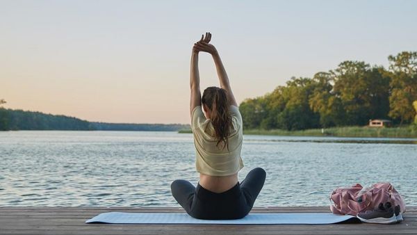 Vrouw zit op een yogamatje op een steiger en strekt zich uit.