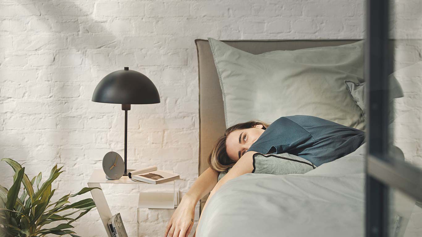 Een goede slaap- of avondroutine is bevorderlijk voor een gezonde slaap. Vrouw ligt zijwaarts op haar bed.