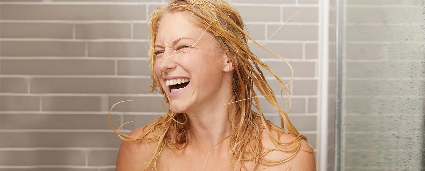 Blonde vrouw in de douche. Ze gooit haar natte haar lachend in het rond.