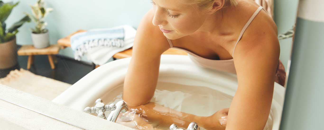 De onderarmen van een vrouw liggen in een met water gevulde wasbak.