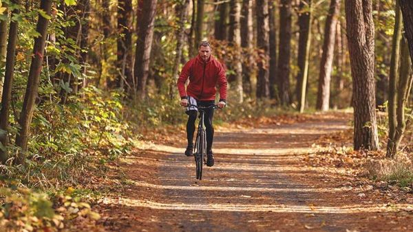 Man in trainingskleren op een fiets in het bos.