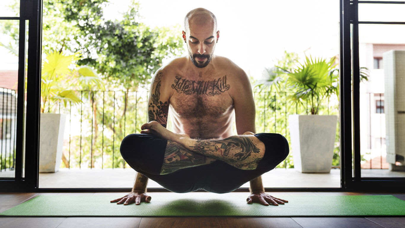 Homme tatoué pratiquant l'assise en tailleur sur les mains.