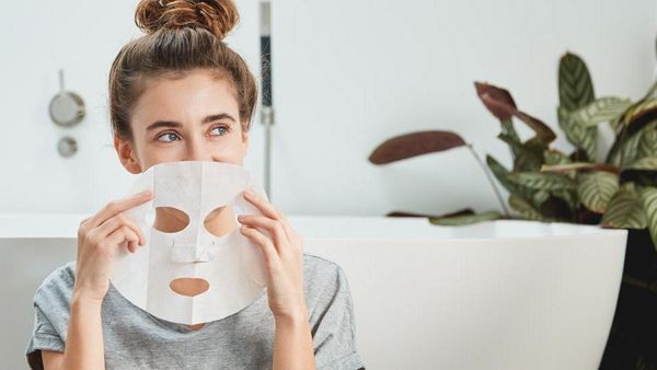 Vrouw zit in de badkamer met een masker voor haar gezicht te lachen.