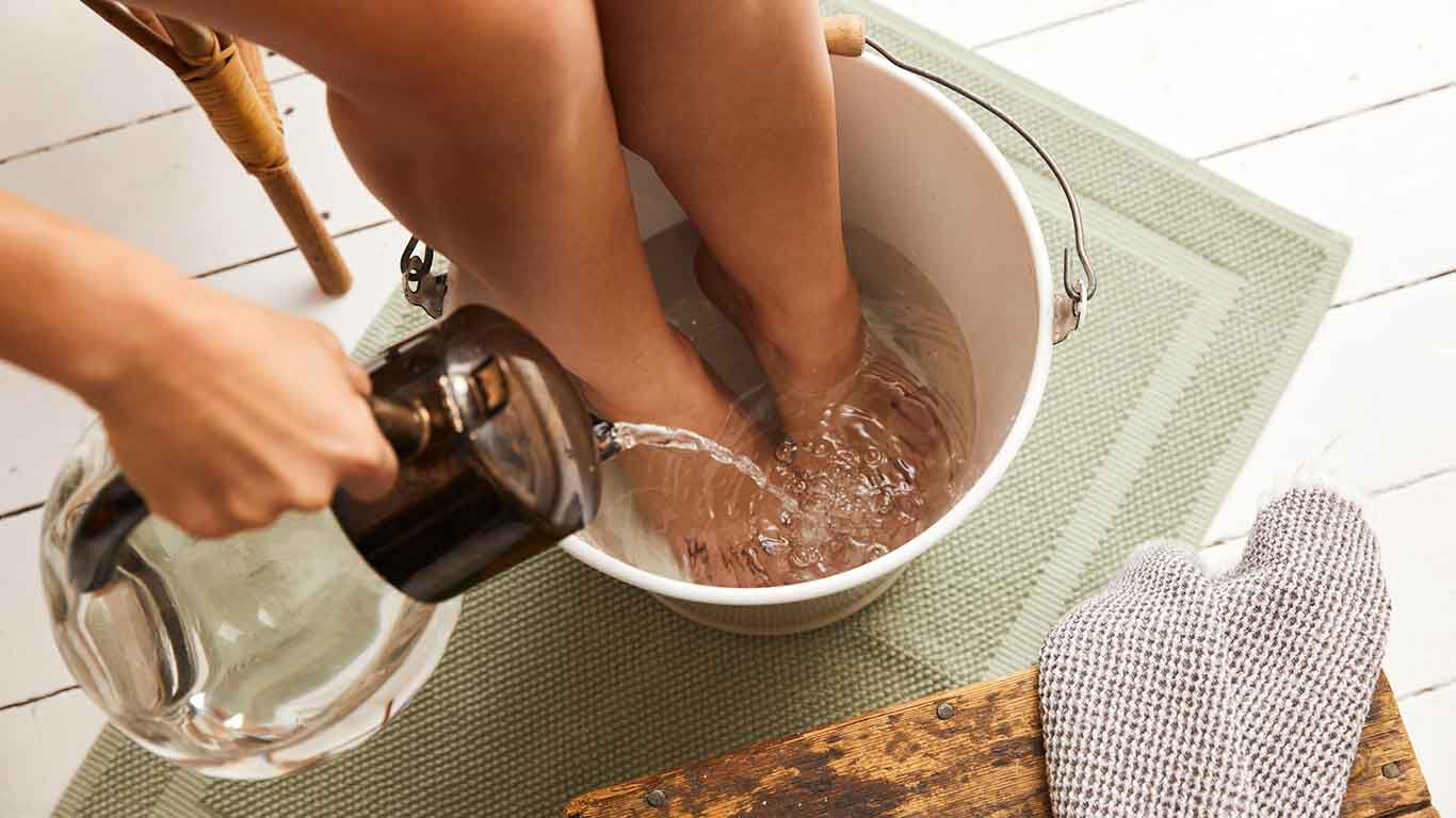 Bain de pieds : les pieds sont plongés dans un seau d'eau. De l'eau neuve est ajoutée dans une carafe en verre.