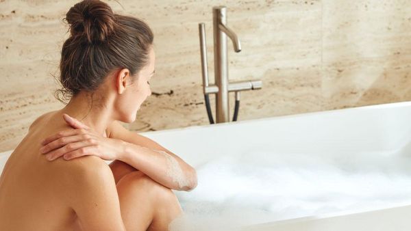 Femme assise dans une baignoire, les jambes repliées.