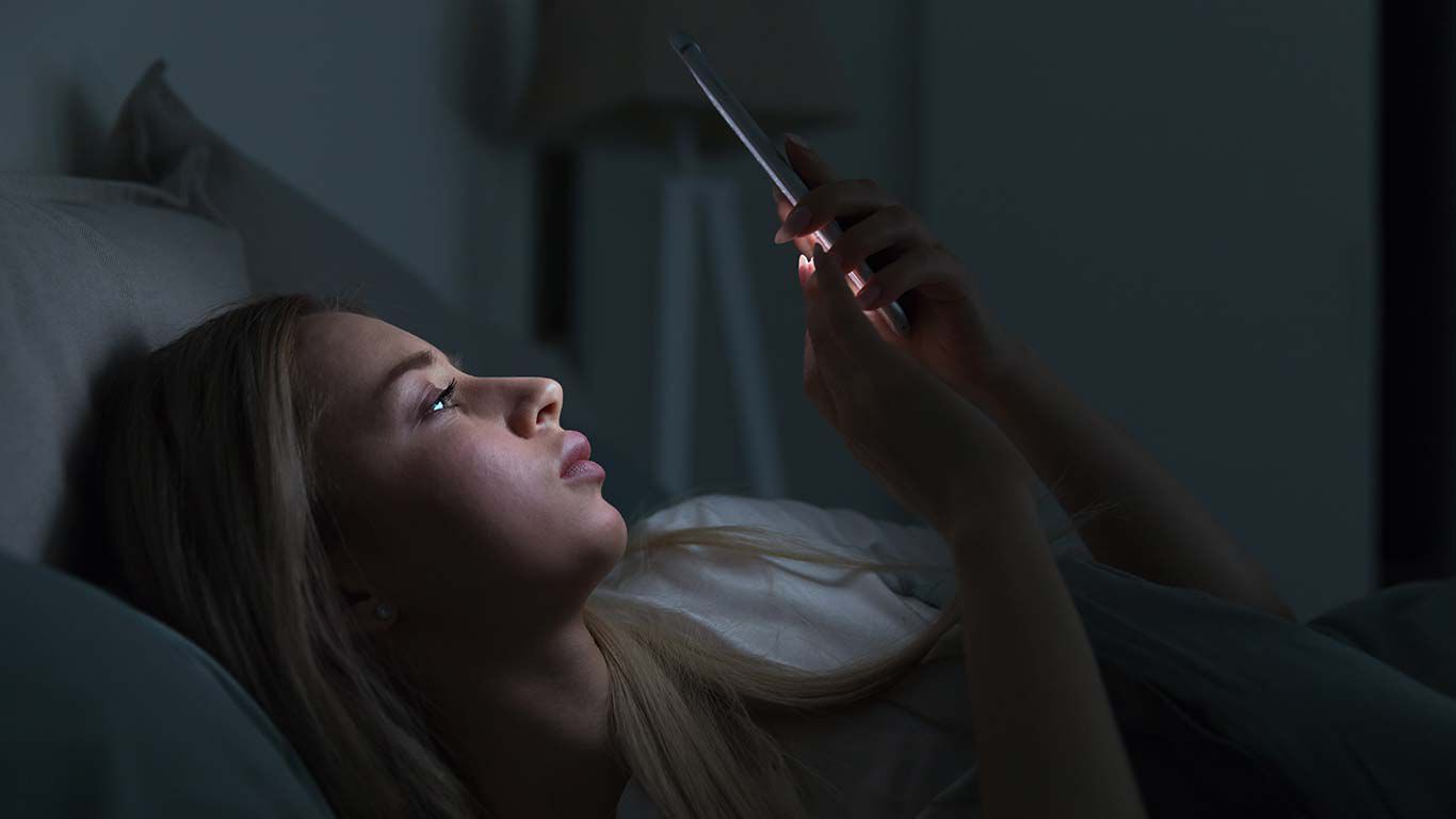 Vrouw ligt in bed met mobiele telefoon