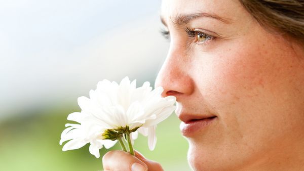Une femme sent une fleur blanche.