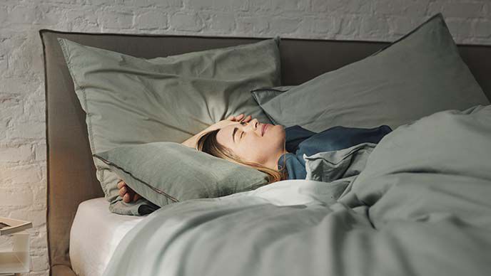 Vrouw ligt in bed en laat de zon op haar gezicht schijnen.