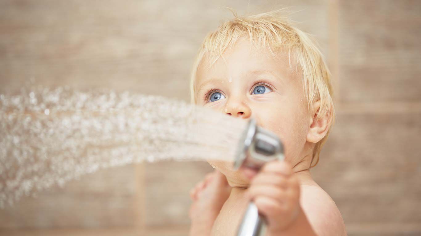 Blonde jongen die een douchekop met water vasthoudt.