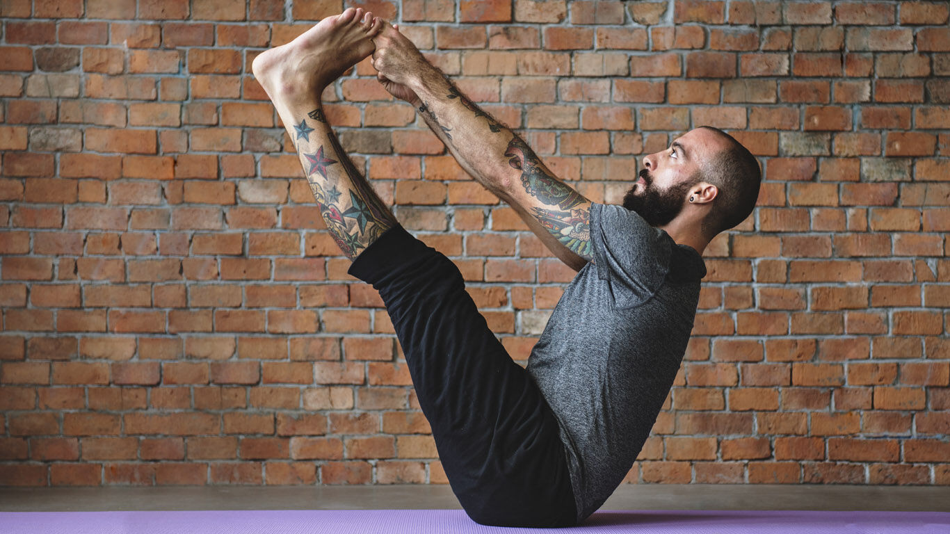 Un homme tatoué effectue un exercice de yoga sur un tapis.