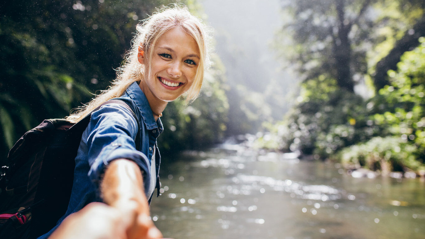 Une femme rayonnante tient la main du photographe au bord d'une rivi&egrave;re.