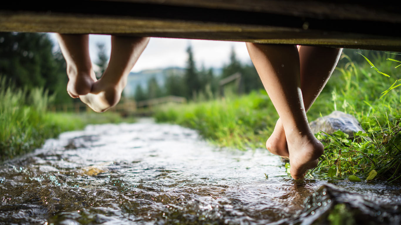 Des pieds se balancent depuis une passerelle. En dessous coule un étroit ruisseau.