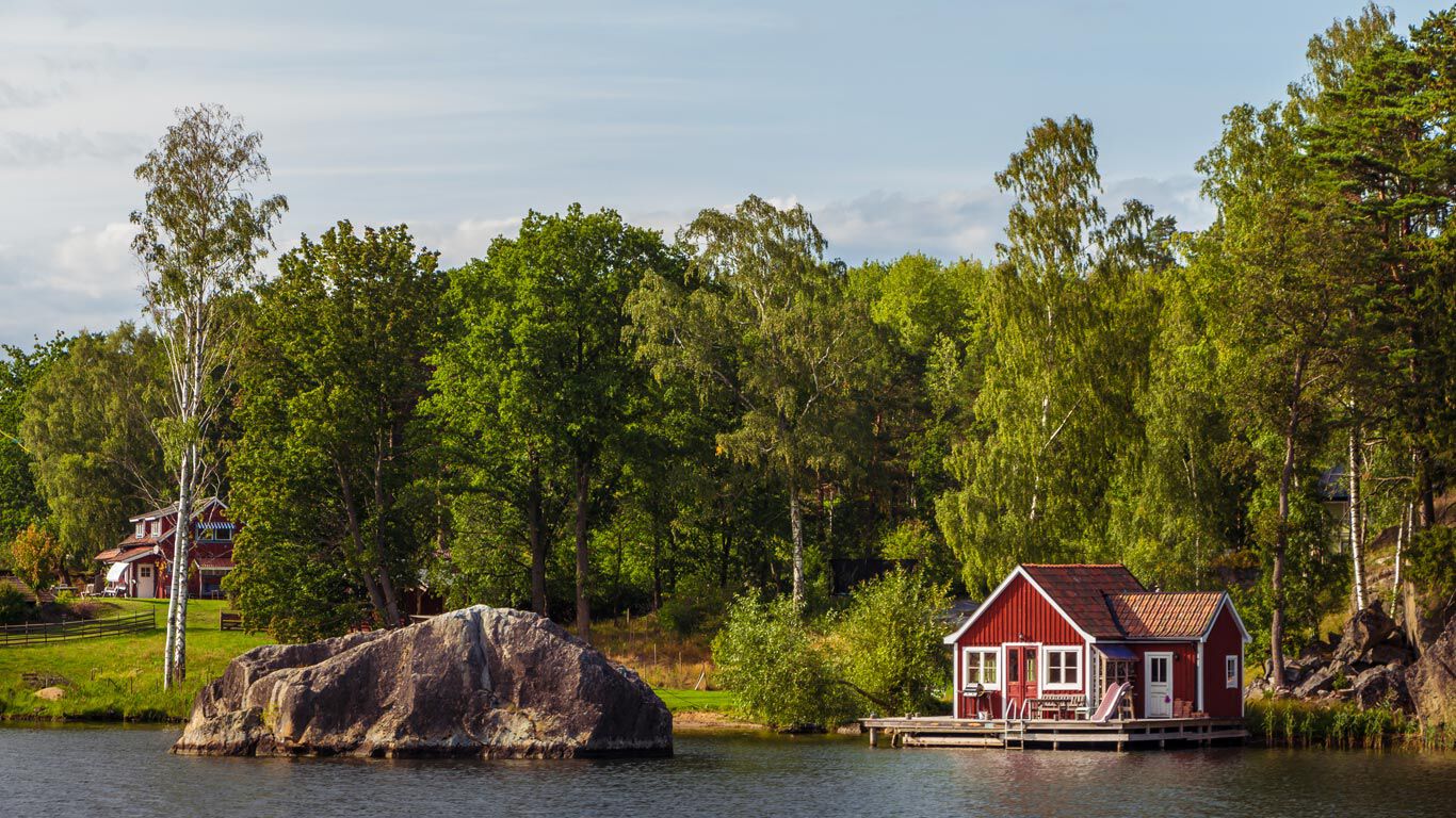 Paysage su&eacute;dois idyllique au bord d'un lac, avec des petites maisons en bois rouges.