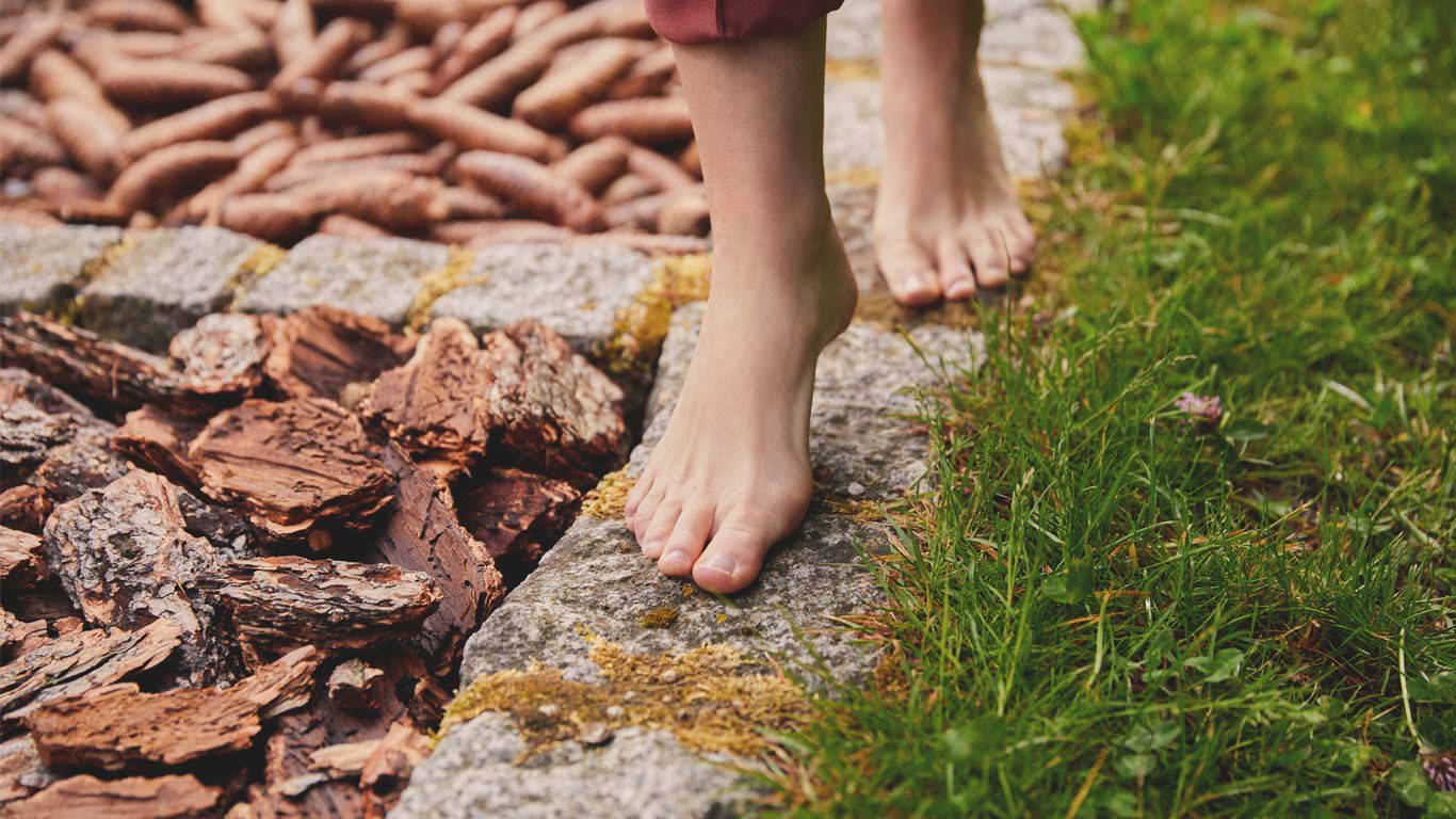 Close-up van voeten die over de stenen rand van een blotevoetenpad lopen.