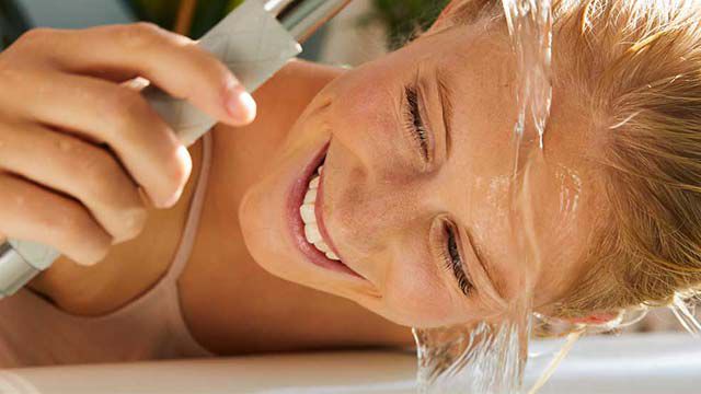 Une femme fait couler de l'eau sur son visage au-dessus de l'évier en riant.