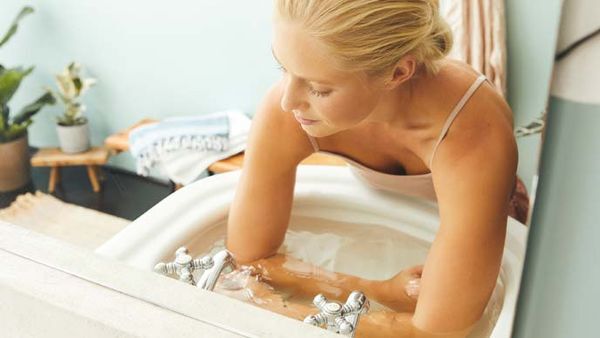 Blonde vrouw doet een koud arm bad in de handbak.