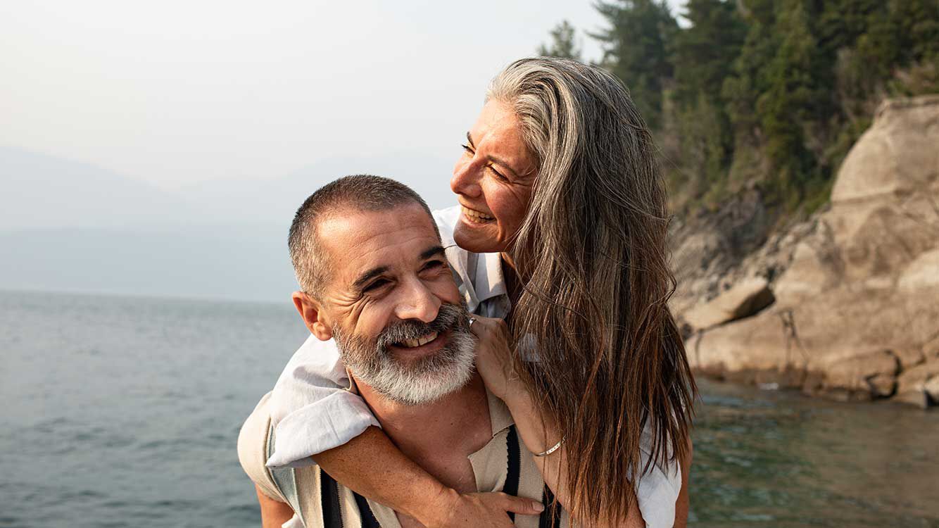 L'homme porte sa femme sur le dos. Ils rient tous les deux. 