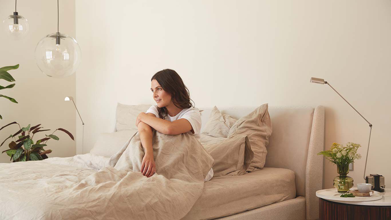 Bruinharige vrouw zit peinzend in haar bed.