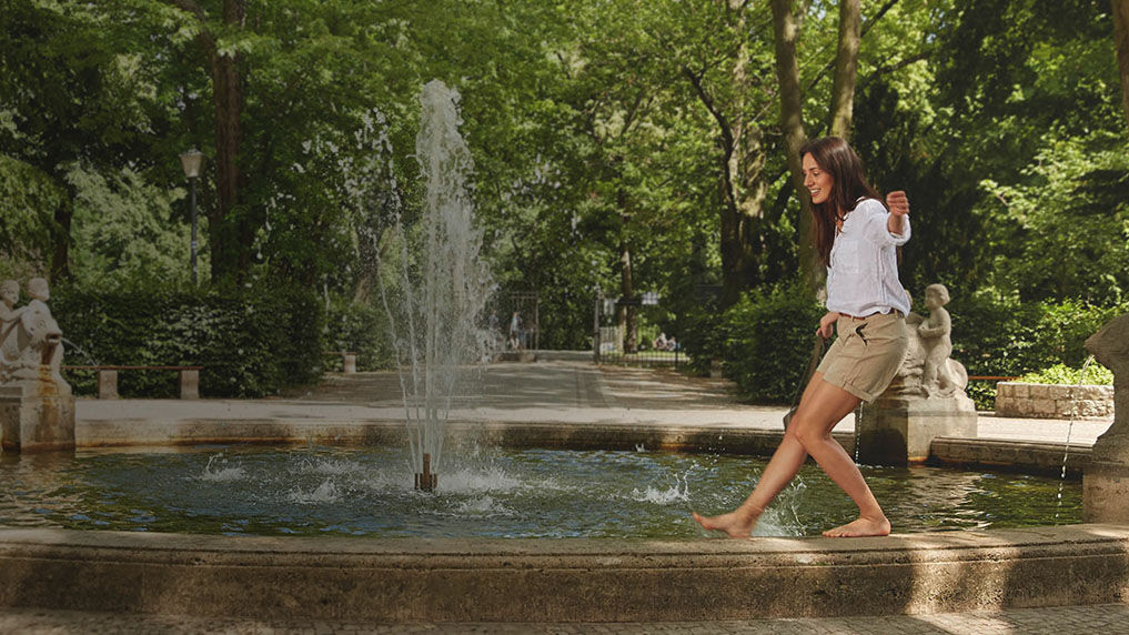Femme en équilibre sur la margelle d'une fontaine, vêtue d'un short et d'un t-shirt.