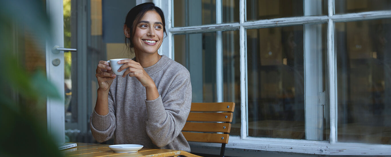 Femme assise près d'une fenêtre ouverte avec une tasse de thé.
