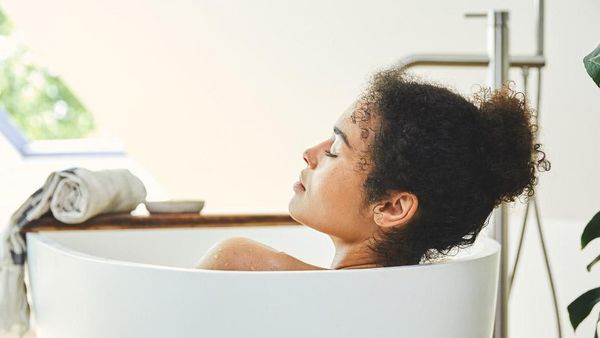 Une femme brune aux cheveux bouclés se détend dans la baignoire.