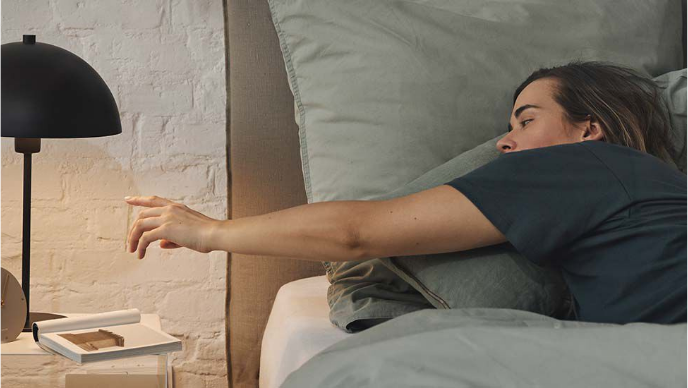 Une femme est allongée dans son lit et s'étire pour attraper une lampe de chevet.