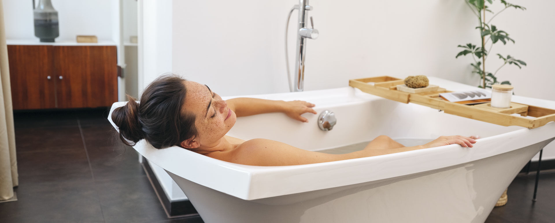 Femme aux cheveux bruns, chignon relev&eacute;, allong&eacute;e et d&eacute;tendue dans la baignoire.