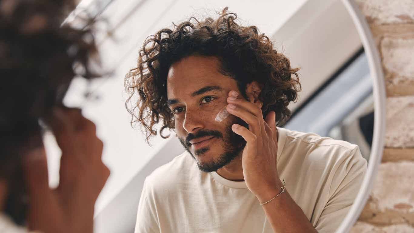 Un homme se tient devant le miroir et s'applique de la cr&egrave;me sur le visage. 