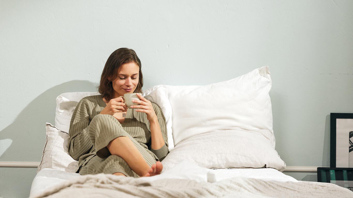 Une femme se d&eacute;tend au lit avec une tasse.