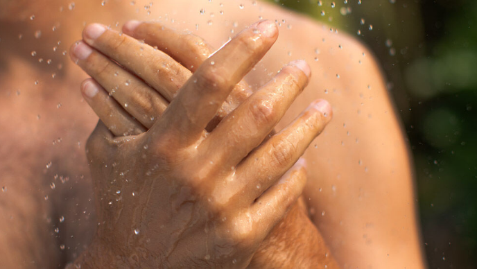 Close-up van twee handen van een man onder de douche. 