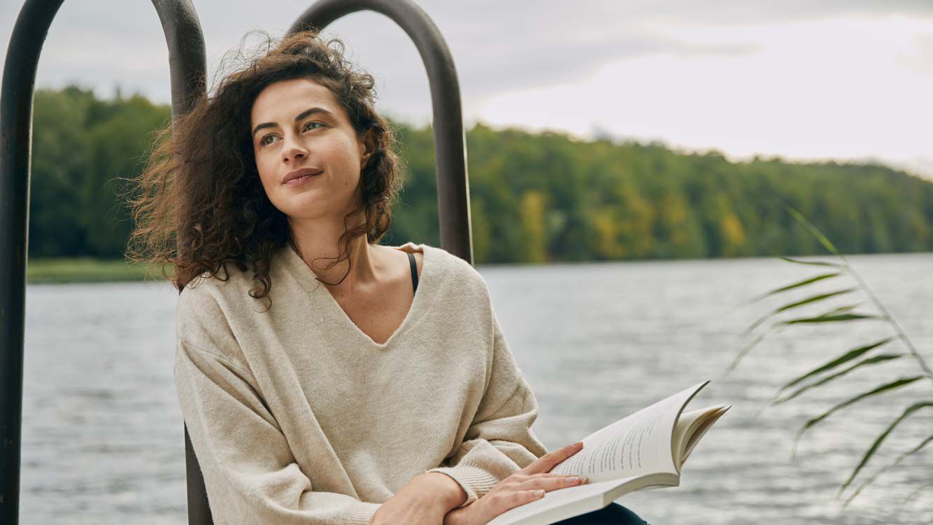 Vrouw ontspant zich met een boek bij het meer. 
