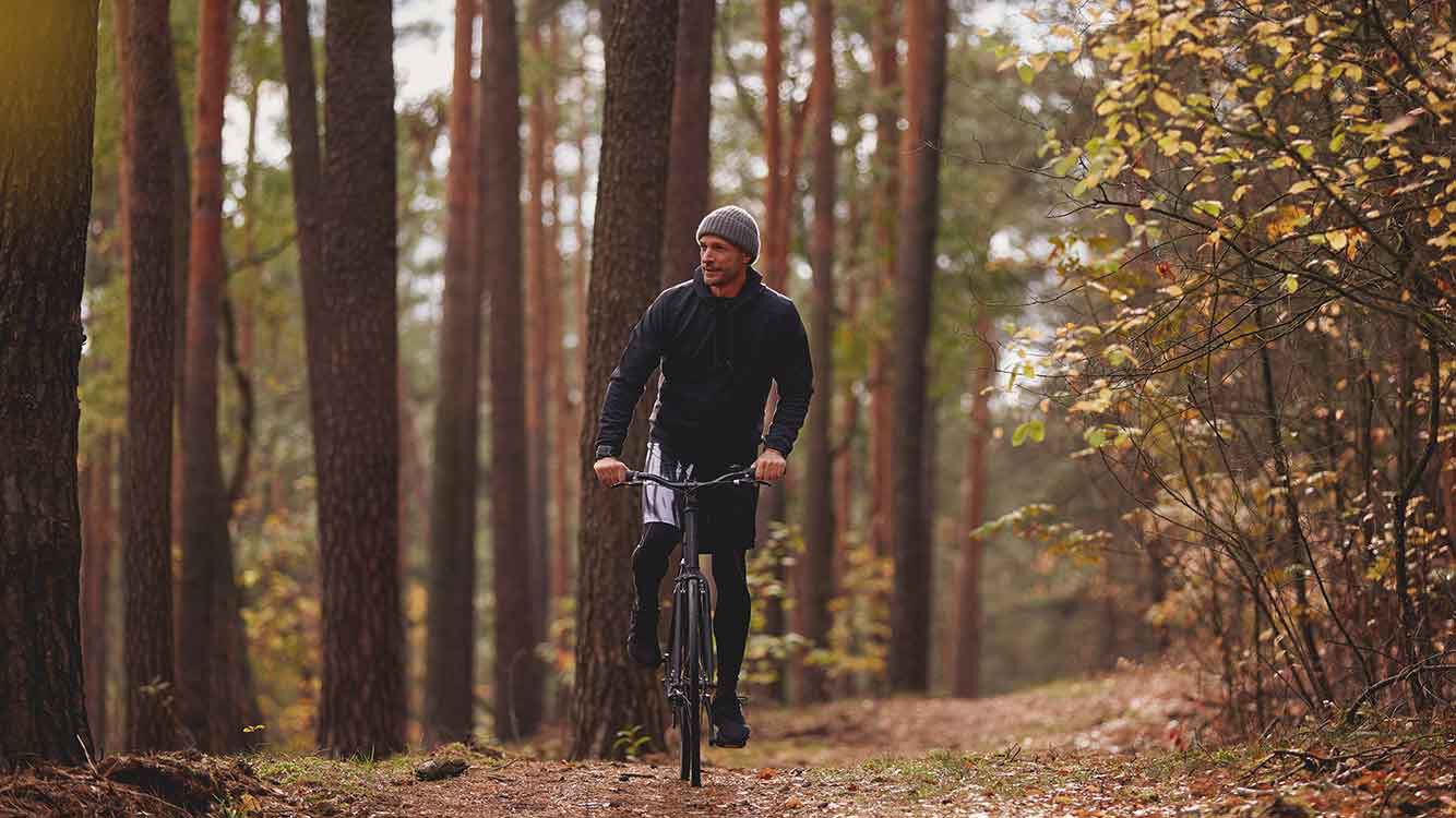 Man in sportkleding rijdt op zijn fiets door het bos.