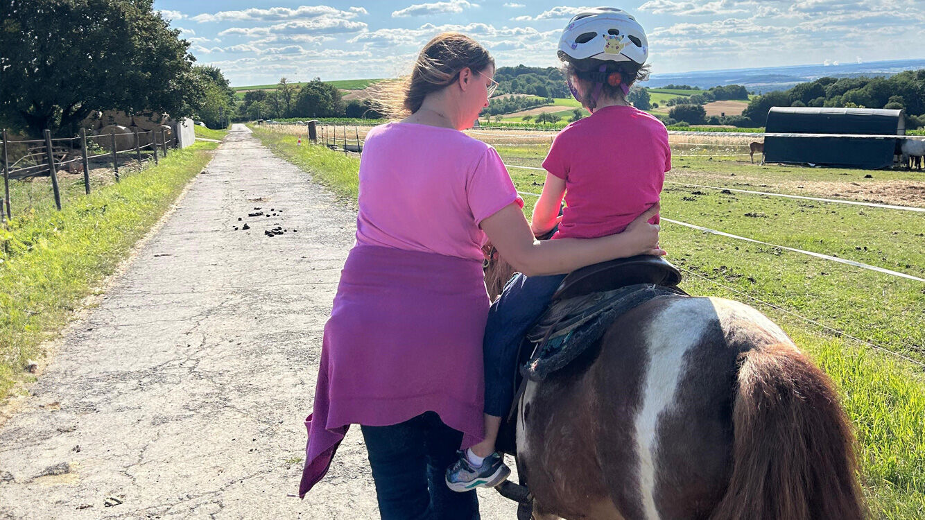 Kind reitet auf einem Pferd und wird dabei von einer Frau geführt