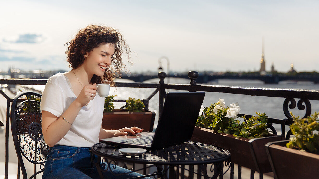 Abverkauf Artikel Frau trinkt Espresso und schaut lächelnd auf ihren Laptop Bildschirm.