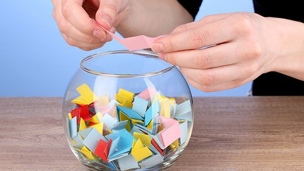 Bunte Lose in einem runden Glas. Eine Hand öffnet ein Los.