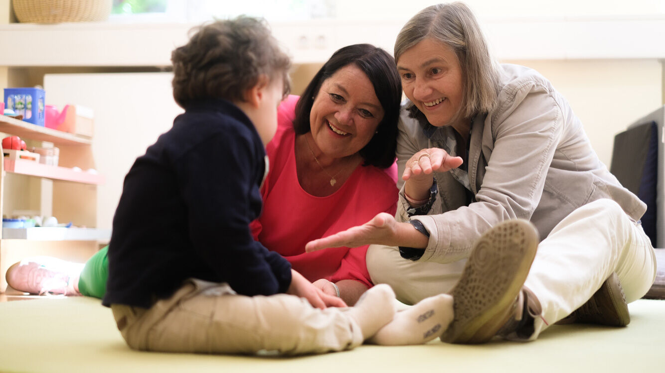 Zwei Frauen sitzen am Boden und spielen mit einem Kleinkind