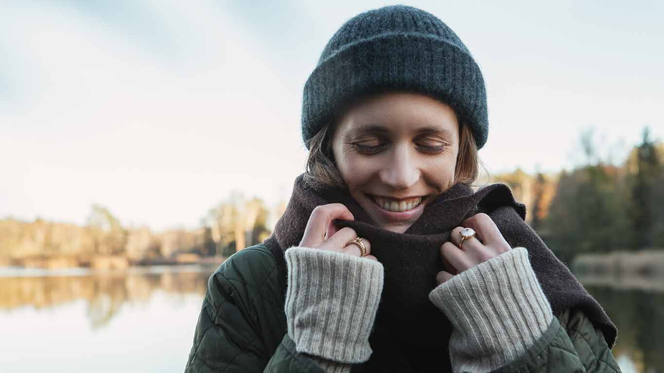 Frau in Winterkleidung. Gesicht in Schal, lachend. 