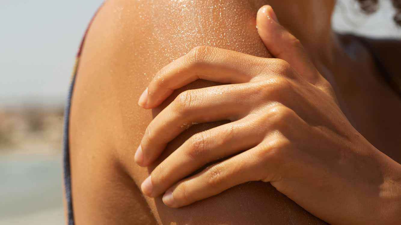 Nahaufnahme einer Hand auf einer Schulter, im Sonnenlicht. 