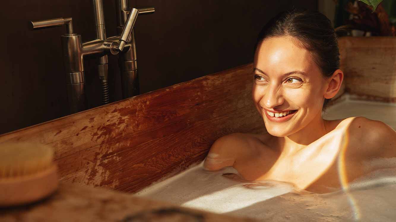 Frau sitzt in der Badewanne und wird von der Sonne angestrahlt. 